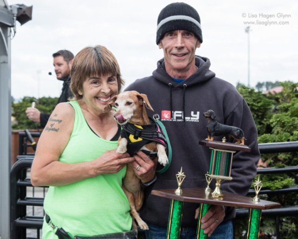 Winning wiener dog "Slinky" with its people and large trophy outside the Winner's Circle