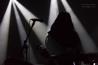 Kelly Lee Owens wears a dark hood and is backlit by white spotlights