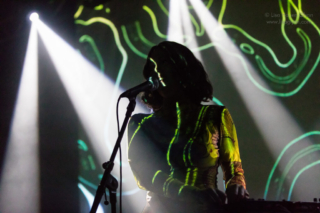 Kelly Lee Owens with visuals projected behind her and onto a stripe on her face