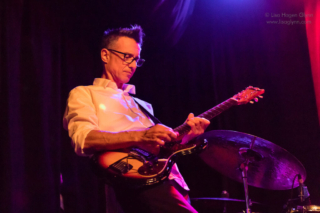 A person wearing glasses plays guitar onstage