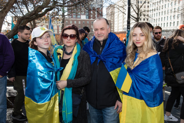 A family wears Ukrainian flags draped around their shoulders.