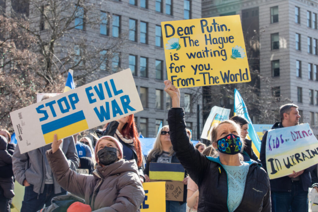 Signs read, "Stop evil war," and "Dear Putin, The Hague is waiting for you."