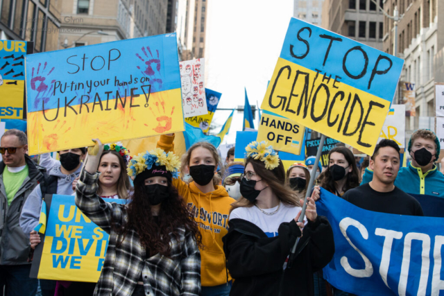 Marchers carry signs that read, "Stop Put-in your hands on Ukraine!" and "Stop the genocide."