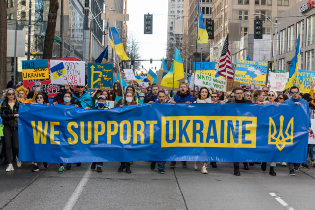 A large crowd marches with a banner that reads, "We support Ukraine."