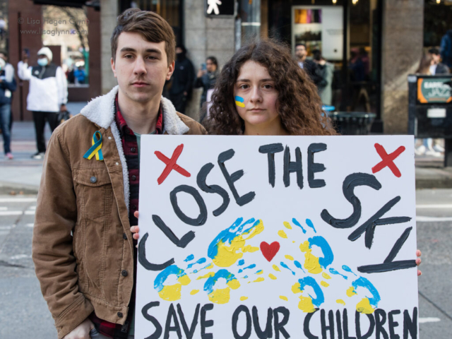 Two people carry a sign that reads, "Close the sky. Save our children."
