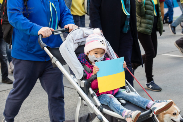 A child in a stroller carries a Ukrainian flag.
