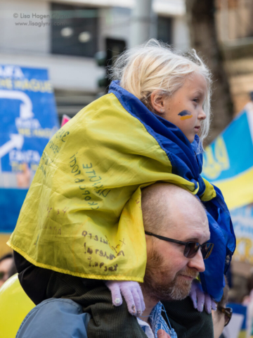 A child rides on shoulders while wearing a blue and yellow flag.
