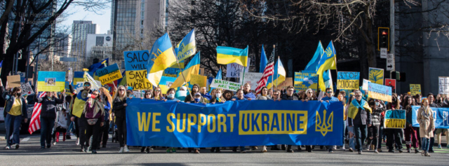 People hold a large blue and yellow banner that reads, "We support Ukraine."