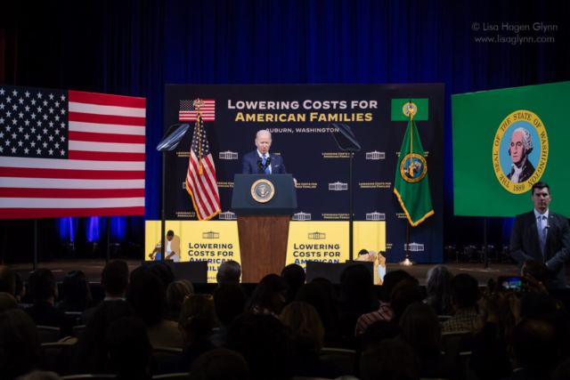 President Joe Biden speaks, flanked by U.S. and Washington flags.