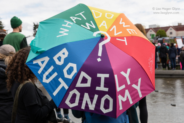 A multicolored umbrella reads, "What do we want? Bodily autonomy"