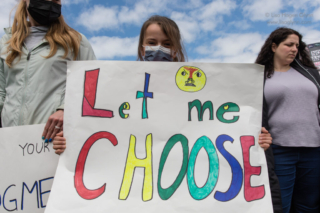 A child holds a sign that reads, "Let me choose"