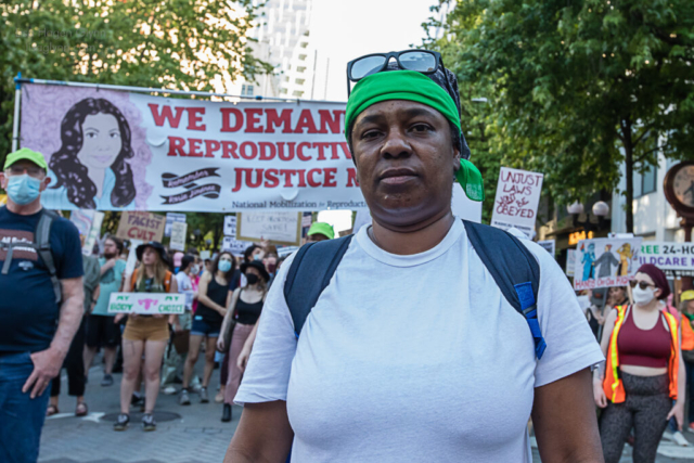 A protester stands in front of a sign that reads, "We demand reproductive justice now."